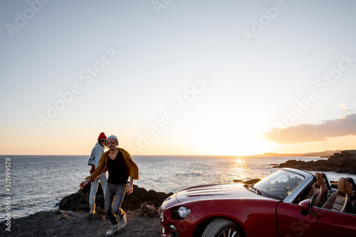 Couple having fun together, enjoying landscapes while traveling by car on the rocky coast, wide view from the side with copy space on the sky