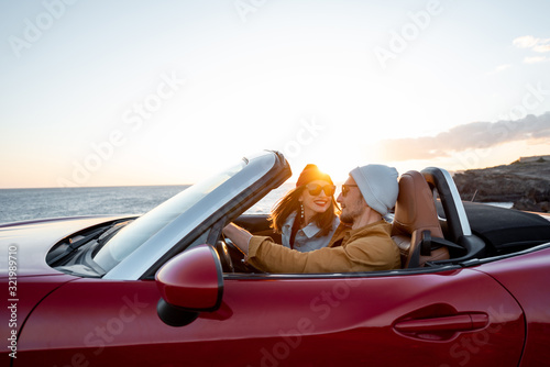 Joyful couple enjoying vacations, driving together convertible car near the ocean on a sunset. Happy vacation, love and travel concept © rh2010