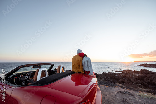 Couple enjoying beautiful views on the ocean, hugging together near the car on the rocky coast, wide view from the side with copy space on the sky © rh2010