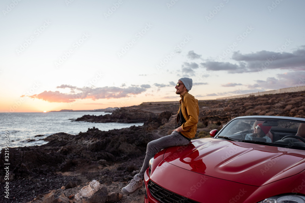 Lifestyle portrait of a man on the rocky coast during a sunset, traveling with woman by car