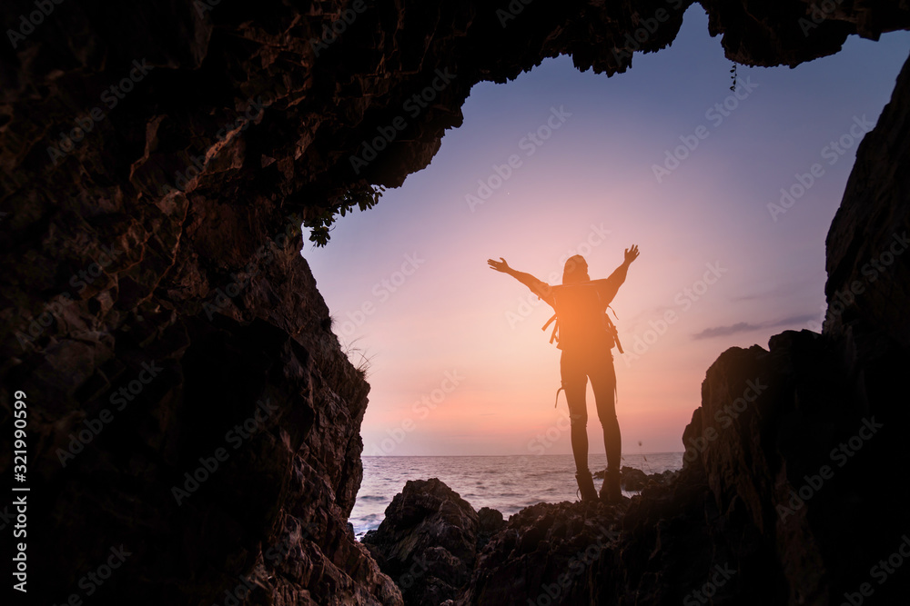 Silhouette of a girl standing in front of the entrance to the cave. Freedom concept. Woman Christians raising their hands in praise and worship.