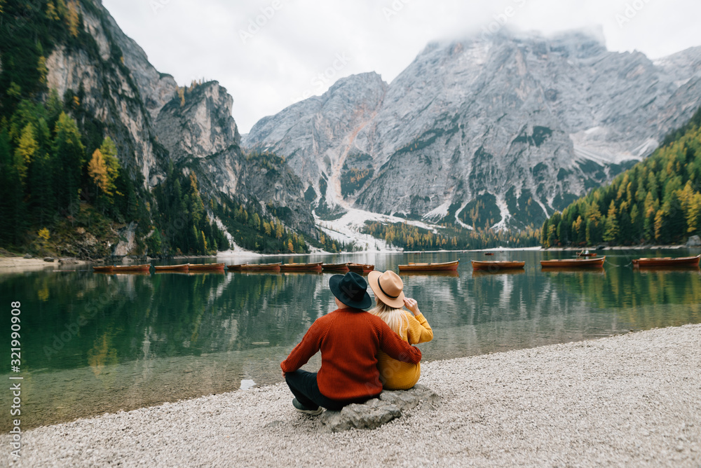 couple in love man and woman are sitting on the shore of lake lago di braies in Italy. men's and women's clothing.