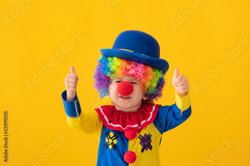 Foto Funny kid clown playing against yellow background