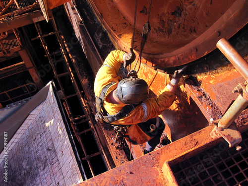 Rope access industrial technician miner fitters, boilermaker wearing fully safety harness, abseiling working maintenance inspecting cleaning chute roller isolated mining iron ore construction Perth