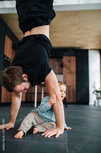 Father exercising, stadning on his hands next to his infant baby