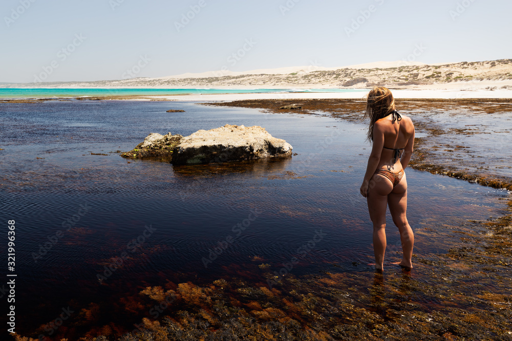 Woman in bikini exploring tannin stained rock pools and coastline during heat wave on the Great Australian Bight in South Australia 