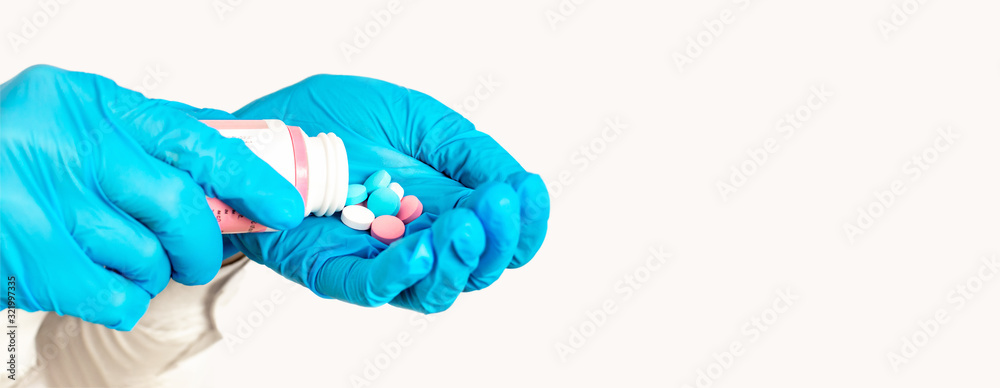 Close-up of hands in blue medical gloves holding a bottle with pills on light background, copy space. The doctor gives a medication, vitamins and antibiotics to treat health in the palm of hand. Close-up of hands in blue medical gloves holding a bottle with pills on light background, copy space. The doctor gives a medication, vitamins and antibiotics to treat health in the palm of hand.
