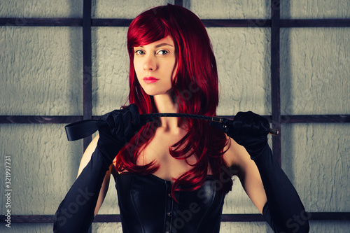 Canvas Print Red-haired girl in a leather corset holds spank.