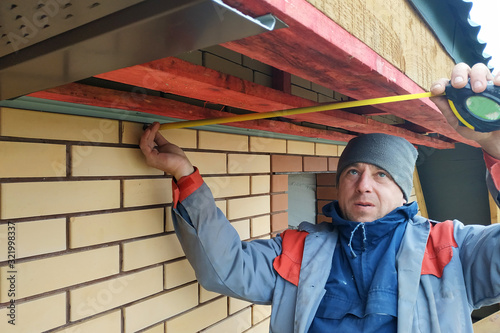 Canvas Print The worker measures the length of the eaves under the roof.2020