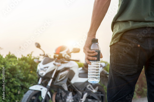 Hand holding bottle water with big bike background,Summer holiday vacation outdoor and view in evening,Drinks, people and lifestyle