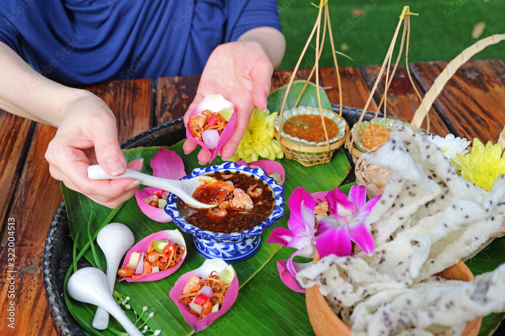 Woman's Hand Holding Fresh Lotus Petal Wrapped Appetizer while Scooping Out Spicy Dip