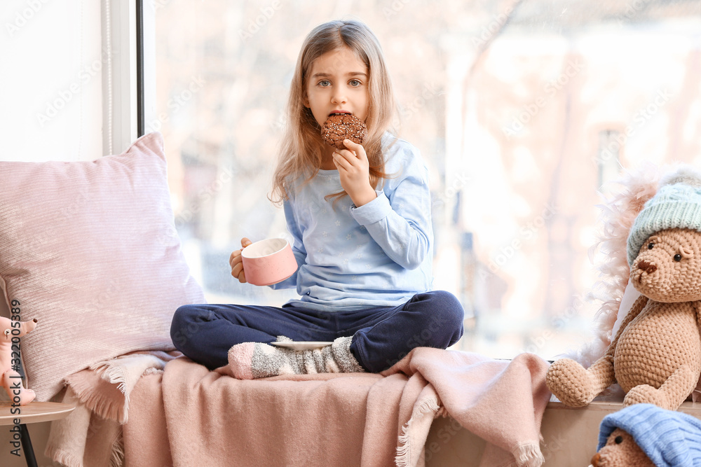 Cute little girl drinking hot chocolate with cookie on window sill at home Cute little girl drinking hot chocolate with cookie on window sill at home