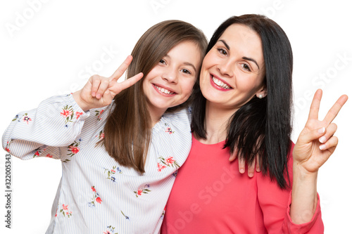 Beautiful young mother and her daughter making peace sign hand gesture, laughing and looking at camera. Isolated over white background. Family love connection concept.