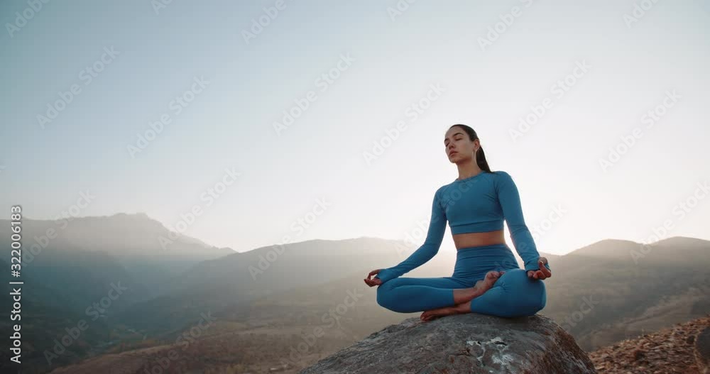 Fit girl doing lotus pose. Young athletic woman meditating in mountains, training and relaxing during sunrise - active lifestyle, zen concept 4k footage Fit girl doing lotus pose. Young athletic woman meditating in mountains, training and relaxing during sunrise - active lifestyle, zen concept 4k footage