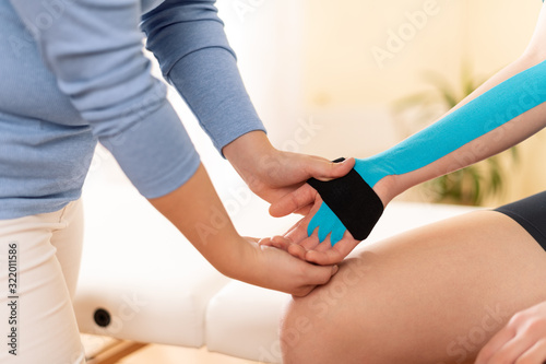 Female physiotherapist applying kinesio tape on patient's arm. Kinesiology, physical therapy, rehabilitation concept. Cropped shot side view. photo