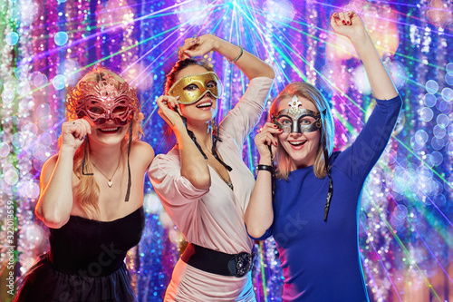 Group of smiling beautiful girlfriends in masks dancing in night club