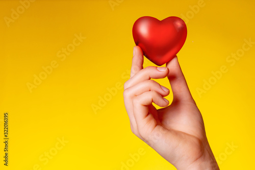 Valentine s day concept. the hand holds a red heart on a yellow-orange background.