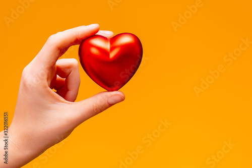 Valentine's day concept. the hand holds a red heart on a yellow-orange background.