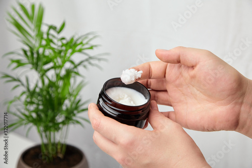 Shea butter in jar, cosmetic skin treatment product. Woman applying moisturizer to her skin of hand