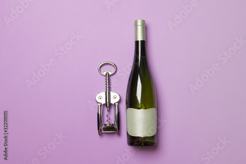 bottle of wine with corkscrew on purple colored paper background