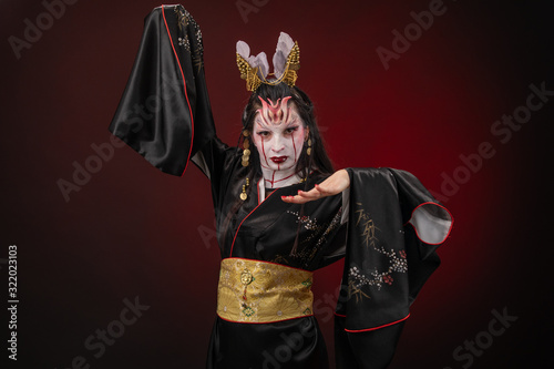 Witchcraft Asian woman in scary Witch ghost story look, mouth blood wound black long hair, studio lighting dark red background. Make up for halloween