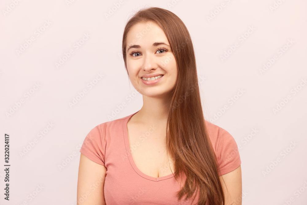 Close up portrait of attractive girl smiling, happy mood positive face expression. Beautiful young woman with long hair clean smooth skin wears pink t-shirt isolated on background in Studio Close up portrait of attractive girl smiling, happy mood positive face expression. Beautiful young woman with long hair clean smooth skin wears pink t-shirt isolated on background in Studio