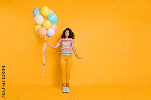 Full length body size view of nice attractive lovely charming cute cheerful cheery wavy-haired girl in striped t-shirt holding air balls isolated on bright vivid shine vibrant yellow color background