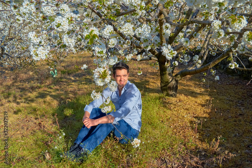 Portrait of a boy posing next to a cherry tree in bloom.