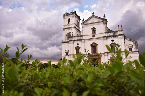 Picture of a white church in goa with a green foreground and cloudy sky