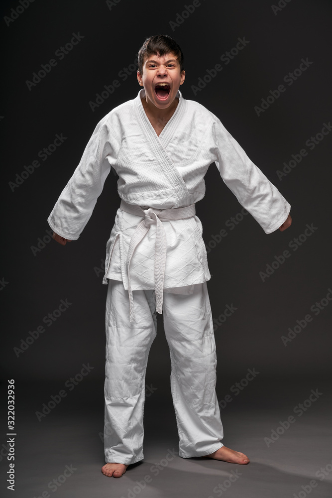 Obraz premium a teenager dressed in martial arts clothing posing and crying on a dark gray background, a sports concept