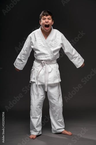 a teenager dressed in martial arts clothing posing and crying on a dark gray background, a sports concept