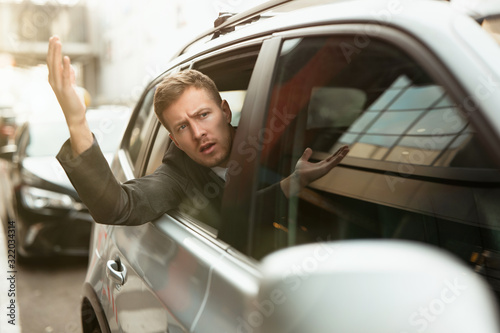young businessman feels nervous looking out from the open car window stuck in traffic jam, big city life photo