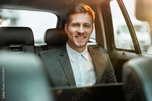 young happy smiling businessman works in his laptop while sitting in his car on his way to office, multitasking concept © studioprodakshn