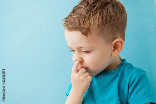 Slika na platnu Little caucasian boy picking his nose on blue background