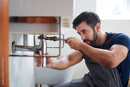 Male Plumber Using Wrench To Fix Leaking Sink In Home Bathroom photo
