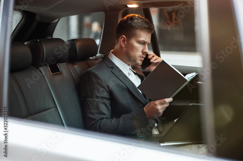 young businessman having phone conversation holds his planner while sitting in his car on the way to meetting with partners, multitasking concept © studioprodakshn