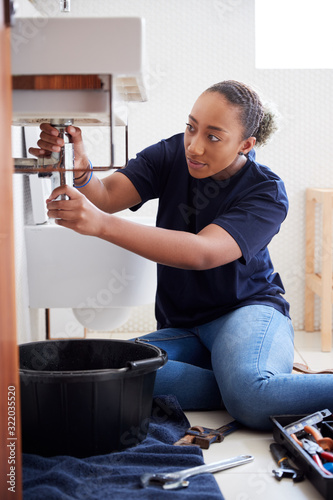 Female Plumber Working To Fix Leaking Sink In Home Bathroom