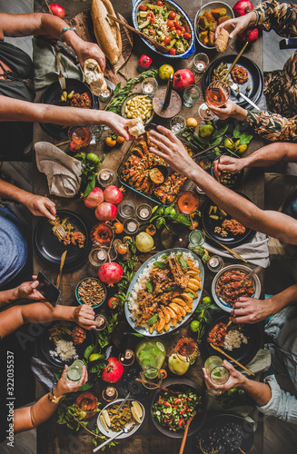 Flat-lay of people feasting with Turkish cuisine lamb chops, quince, bean, vegetable salad, babaganush, rice pilav, pumpkin dessert, lemonade over rustic table, top view. Middle East cuisine