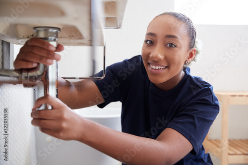Portrait Of Female Plumber Working To Fix Leaking Sink In Home Bathroom