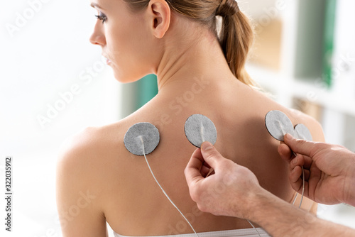 Therapist setting electrodes on back of beautiful woman during electrode treatment photo