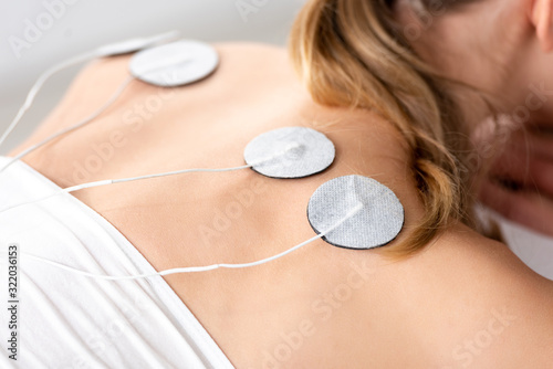 Cropped view of woman with electro stimulation electrodes on back on grey background photo