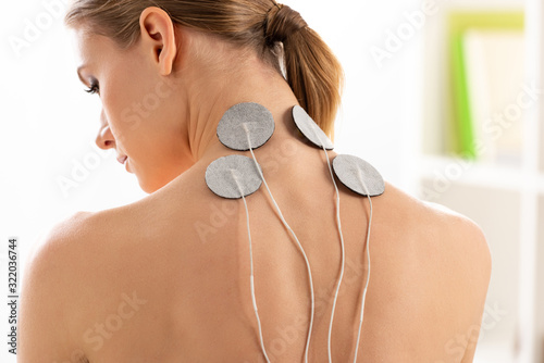 Back view of beautiful woman with electrodes on neck during electrotherapy in clinic photo