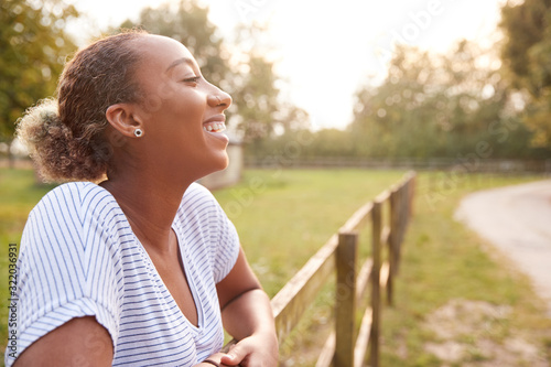 Φωτογραφία Smiling Young Woman Taking A Break And Resting On Fence During Walk In Countrysi