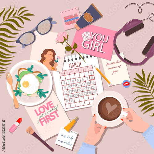 Women's business layout. Flat lay desk style, female hands hold mug with coffee, motivational posters with feminist quotes calendar for march month, pen, cosmetics, headphones, glasses and plants.