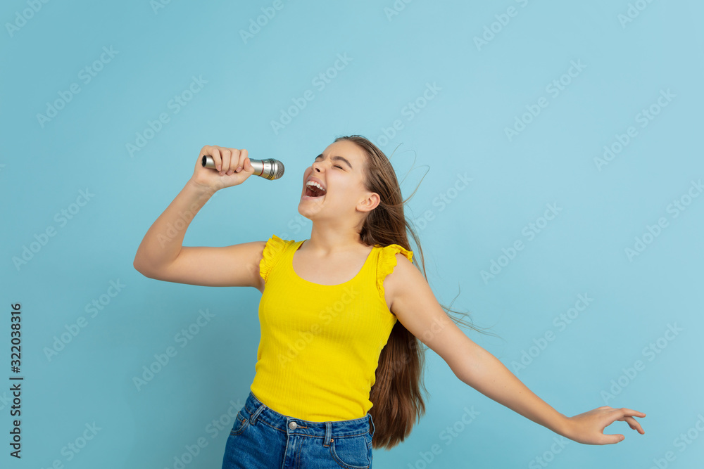Singing like celebrity. Caucasian teen girl's portrait isolated on blue background. Beautiful long hair model in casual. Concept of human emotions, facial expression, sales, ad. Copyspace. Looks cute. Singing like celebrity. Caucasian teen girl's portrait isolated on blue background. Beautiful long hair model in casual. Concept of human emotions, facial expression, sales, ad. Copyspace. Looks cute.