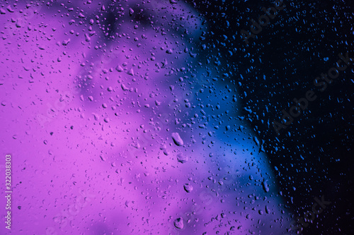 Drops of water (rain) on the glass, illuminated by neon light purple and blue, cyberpunk background photo