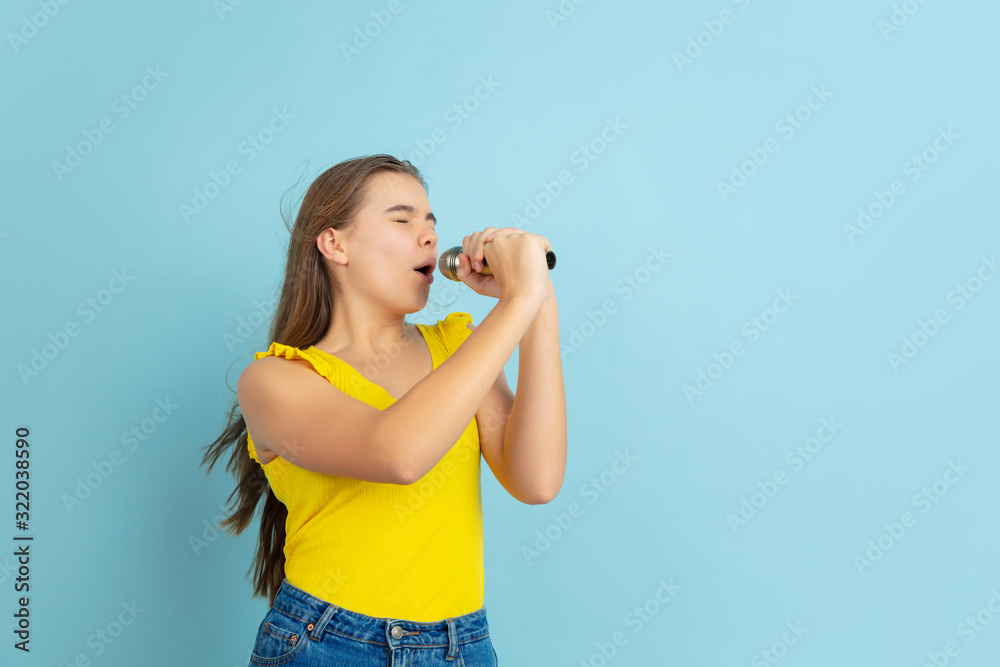 Singing like celebrity. Caucasian teen girl's portrait isolated on blue background. Beautiful long hair model in casual. Concept of human emotions, facial expression, sales, ad. Copyspace. Looks cute. Singing like celebrity. Caucasian teen girl's portrait isolated on blue background. Beautiful long hair model in casual. Concept of human emotions, facial expression, sales, ad. Copyspace. Looks cute.