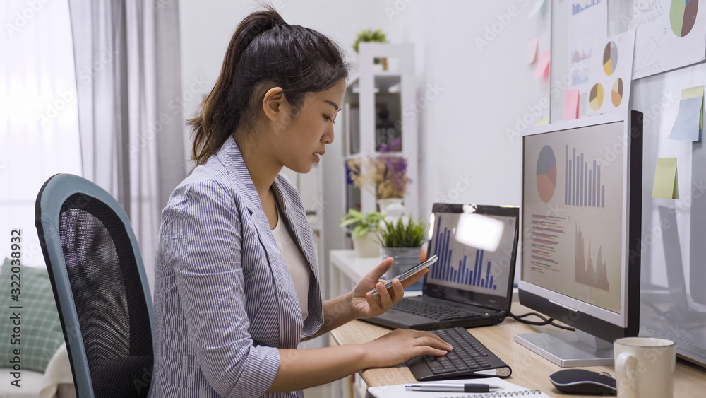 Young elegant asian chinese business woman sitting in home office at table and using smartphone. focus side view beautiful girl employee holding mobile phone checking online website during day. Young elegant asian chinese business woman sitting in home office at table and using smartphone. focus side view beautiful girl employee holding mobile phone checking online website during day.