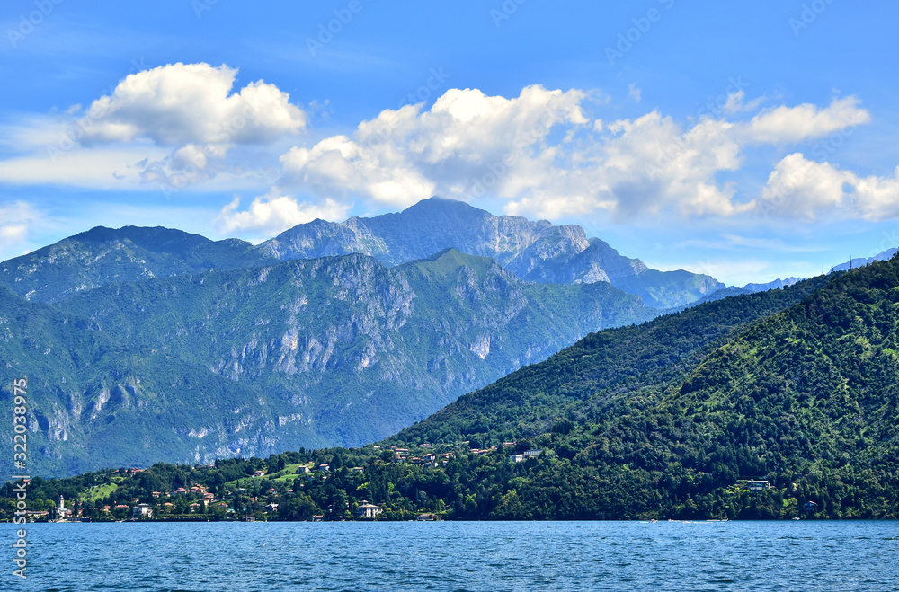 Lake Como in the Lombardy region of Italy, green alpine mountains covered with trees, a small town in the distance, a villa and a beautiful garden, in the summer afternoon.