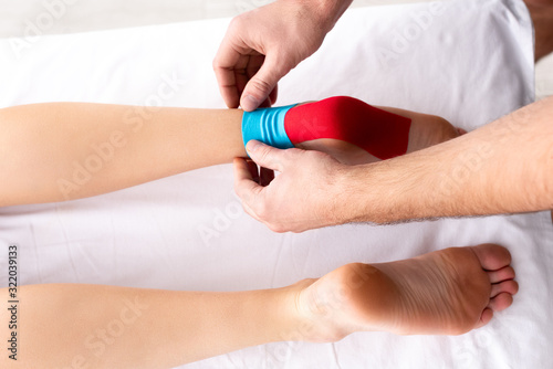 Top view of doctor applying kinesiology tapes on feet of patient on massage couch